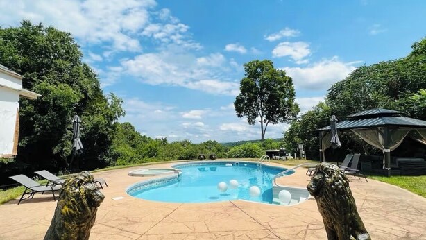 Una piscina con dos estatuas de leones, rodeada por una zona de patio con sillones reclinables y un área de estar cubierta.