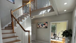 Un vestíbulo amplio con una escalera de madera, una obra de arte con un mapa del mundo y un tapete de bienvenida.