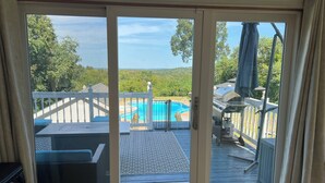 Puerta corredera de vidrio que da a una terraza con piscina, muebles de exterior y una parrilla.