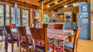 A rustic dining area with wooden tables and chairs, a brick wall, and a kitchen with a brick oven.