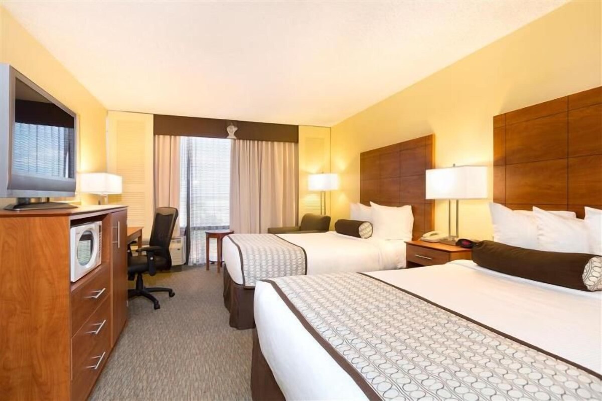 A hotel room with two beds, a desk, a chair, a TV, and a minibar.