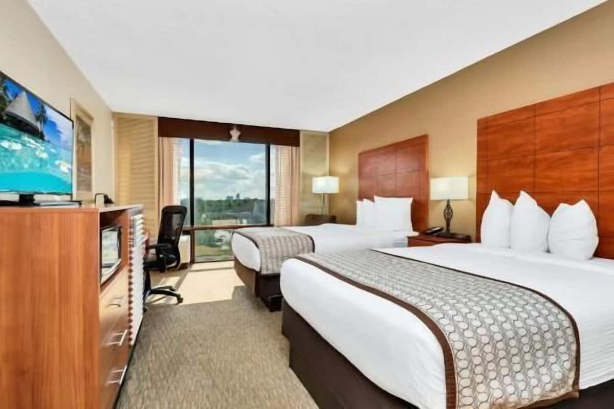 A hotel room with two beds, a TV, a desk, and a view of the city.
