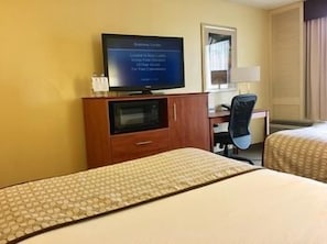 Habitación de hotel con dos camas, un televisor sobre un mueble de madera, un escritorio con una silla y un espejo.