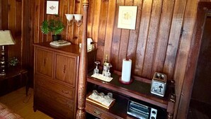Une pièce aux murs lambrissés, contenant un lit, une commode, une radio et des tableaux encadrés.