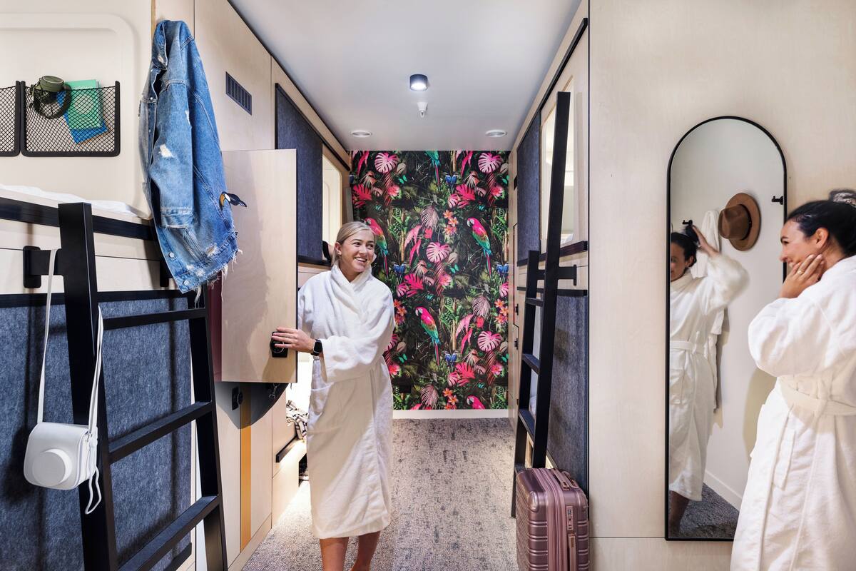 A hotel room with a bed, a mirror, a suitcase, and a floral wallpaper.