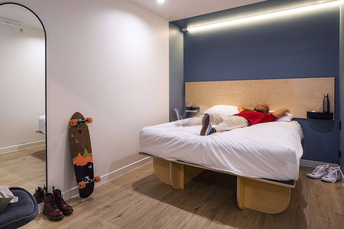 A modern bedroom with a bed, a large mirror, a skateboard, and a pair of shoes.