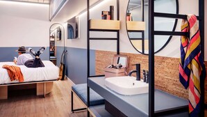 Una habitación de hotel moderna con literas, un escritorio pequeño, un lavamanos y un espejo.