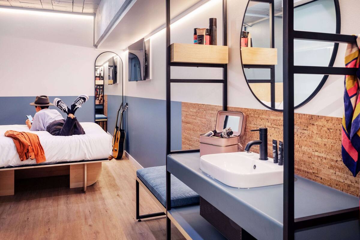 A modern hotel room with a bunk bed, a small desk, a sink, and a mirror.