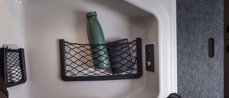 A white bathroom with a black mesh shelf holding a green water bottle and a black object, possibly a phone or remote.