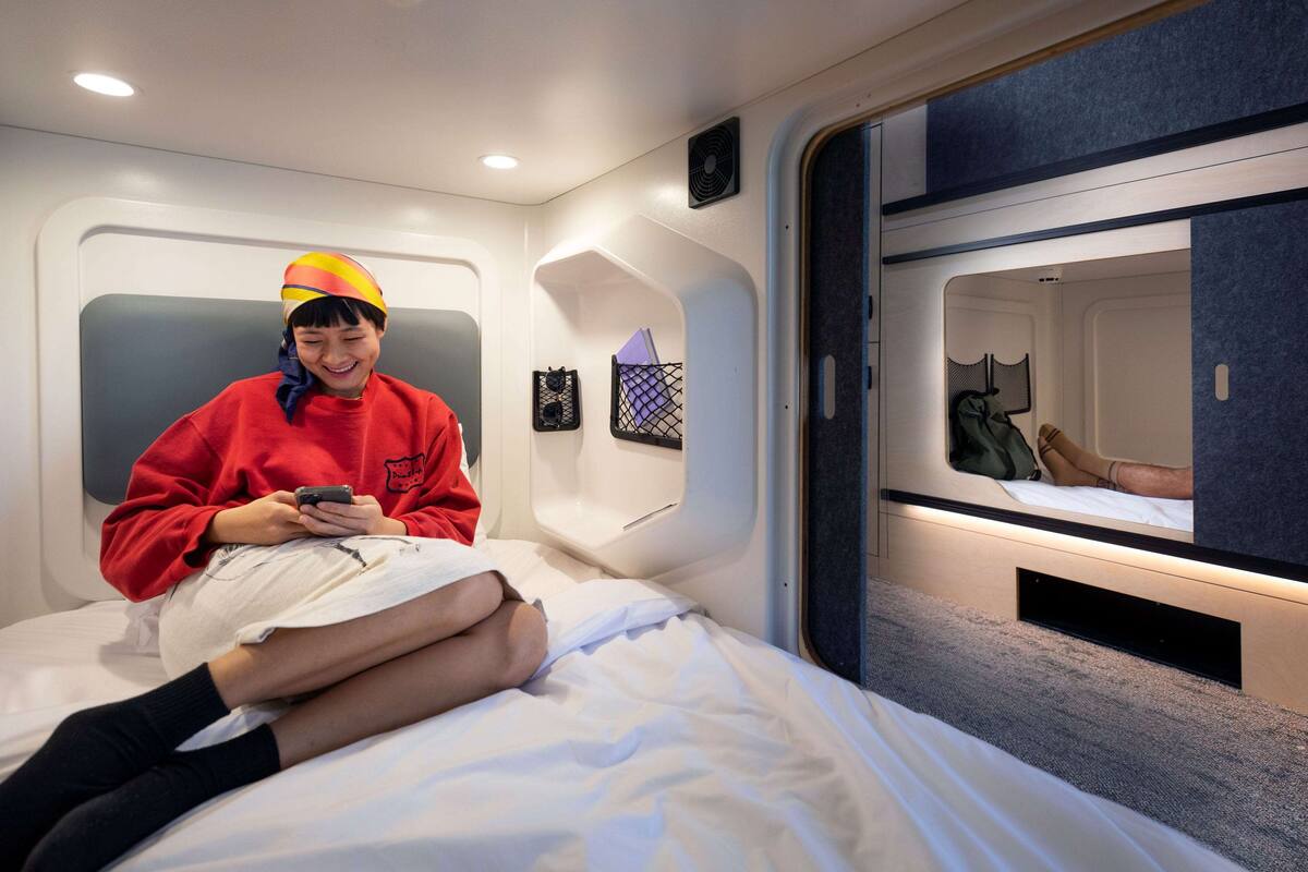 A modern interior with a bed, a person using a mobile phone, and a small window with a view of another room.