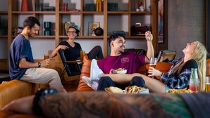 Un grupo de personas sentadas en un sofá en una habitación con una estantería y un cuadro en la pared.