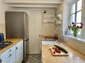 Ett modernt kök med ett kylskåp i rostfritt stål, en bänkskiva i trä och ett fönster med utsikt.