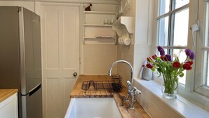 Eine kompakte Küche mit einem Edelstahl-Kühlschrank, einer Holz-Arbeitsplatte, einem Spülbecken mit Armatur und einem Fenster mit einer Tulpenvase.