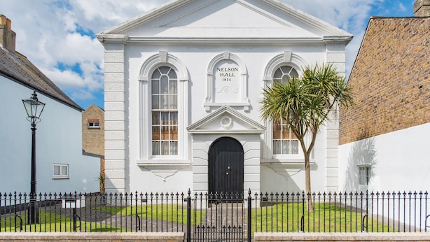 Un edificio blanco con ventanas arqueadas y una puerta negra, con la inscripción "Nelson Hall 1814".