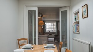 Un comedor con una mesa de madera dispuesta para cuatro, sillas y vistas a una sala de estar con un sofá y una ventana.