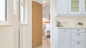 A hallway leading to a bedroom with a wooden door, a bed with white bedding, and a kitchen area with white cabinets and a countertop. - The perfect retreat for couples wanting to enjoy Deal (Deal)
