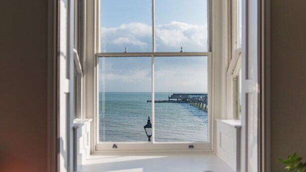 A window with a view of the sea and a pier. - Light, bright, and colourful apartment opposite Deal pier (Deal)