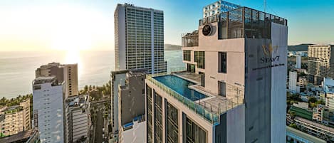 Un hotel de gran altura con piscina en la azotea, vista al mar y un letrero que indica Stay7 International Hotel.