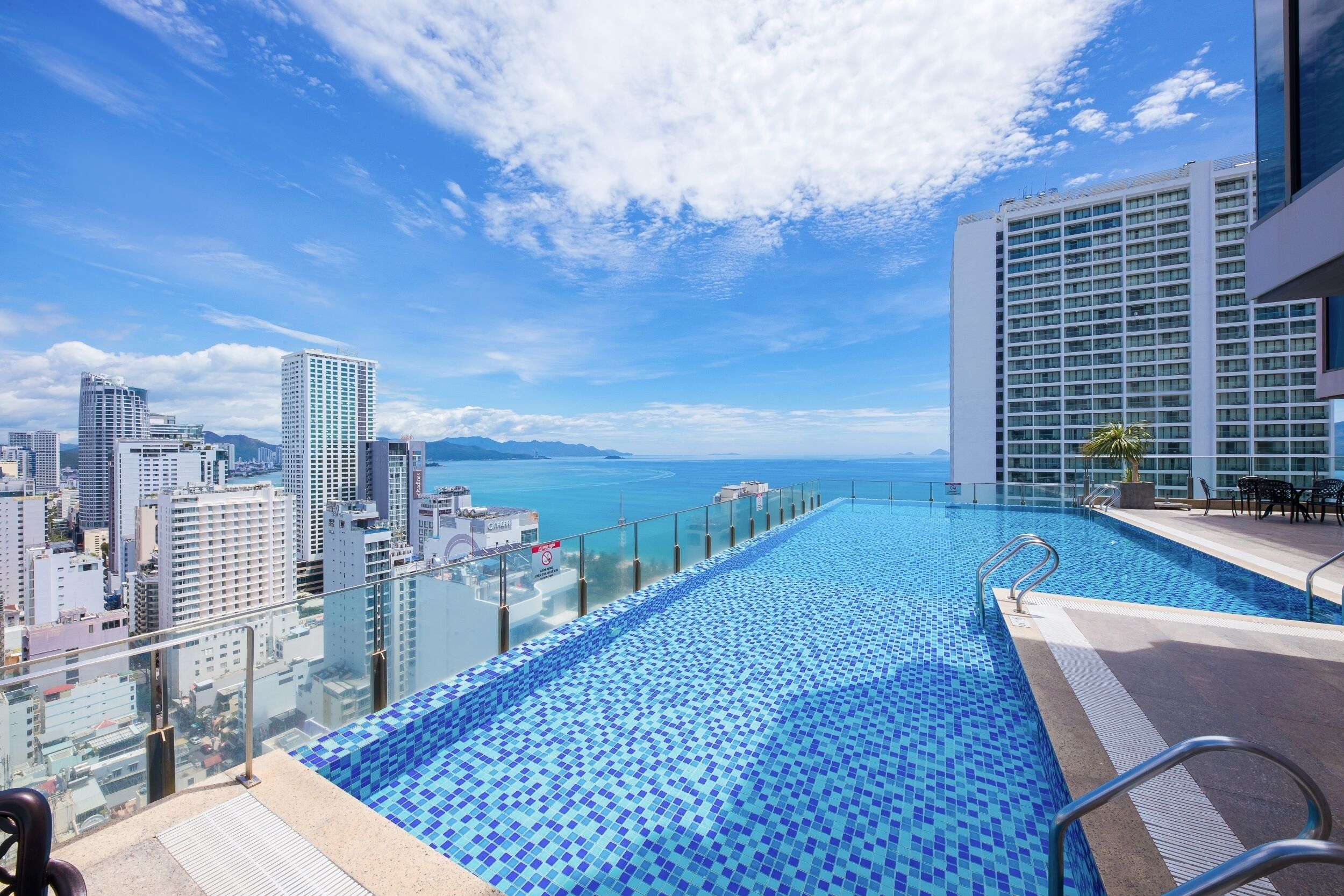 Piscina infinita no terraço com vista para a cidade, guarda-corpos de vidro e céu claro.
