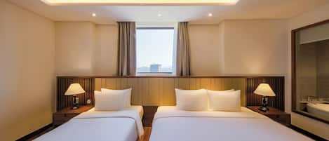 A hotel room with two beds, a large window with curtains, a nightstand with a lamp, and a bathroom with a mirror.