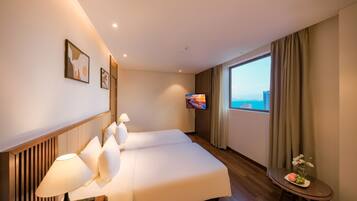 A hotel room with a large bed, a TV, a small table with flowers, and a view of the city.
