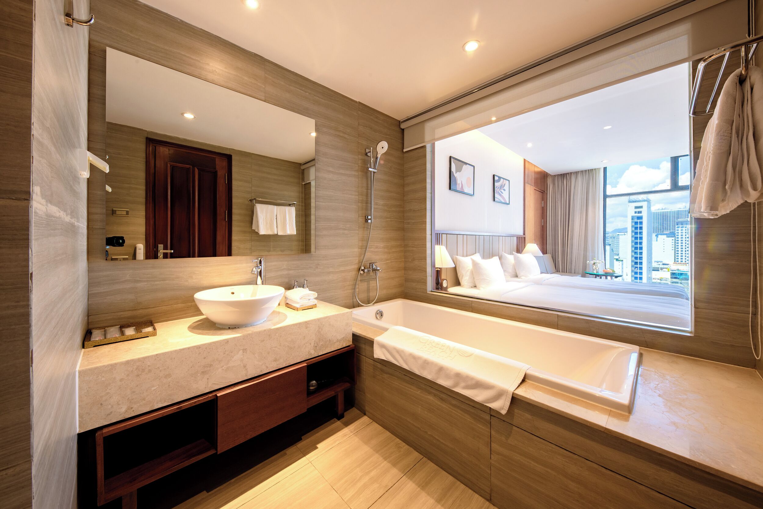 A modern bathroom with a large mirror, a sink, a bathtub, and a window with a city view.