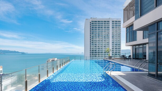 Ein Pool ohne Rand auf dem Dach mit freiem Blick auf das Meer und einem Hochhaus im Hintergrund.