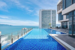 Une piscine à débordement située sur le toit, offrant une vue dégagée sur la mer et un immeuble de grande hauteur en arrière-plan.