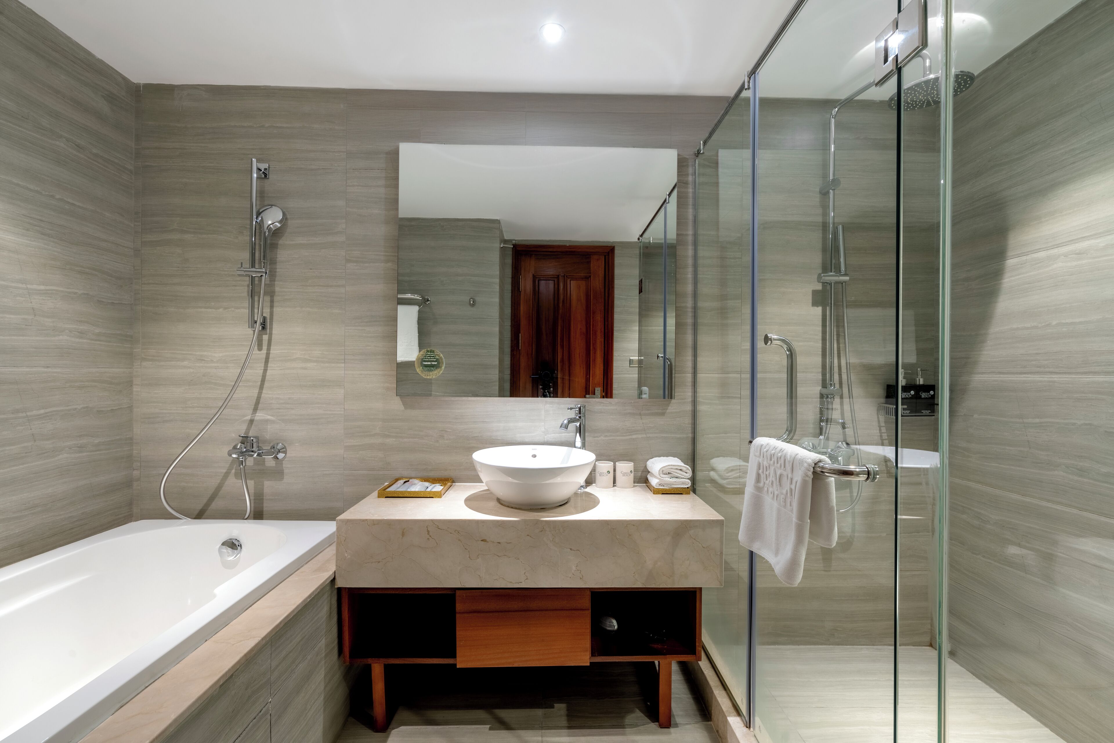 Un baño moderno con una bañera independiente, un tocador espacioso con encimera de mármol, ducha con mampara de vidrio y puerta de madera.