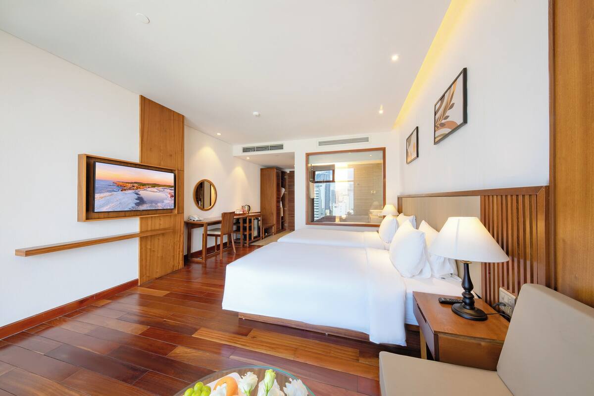 A hotel room with a large bed, a desk, a chair, a TV, and a view of the city.