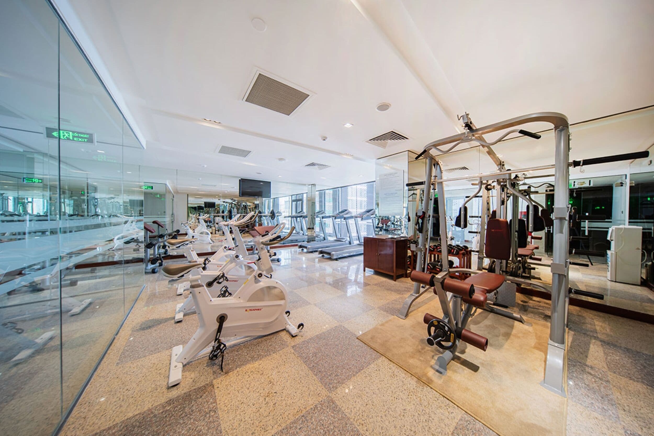 A modern gym with various exercise equipment, glass walls, and a clean, spacious layout.