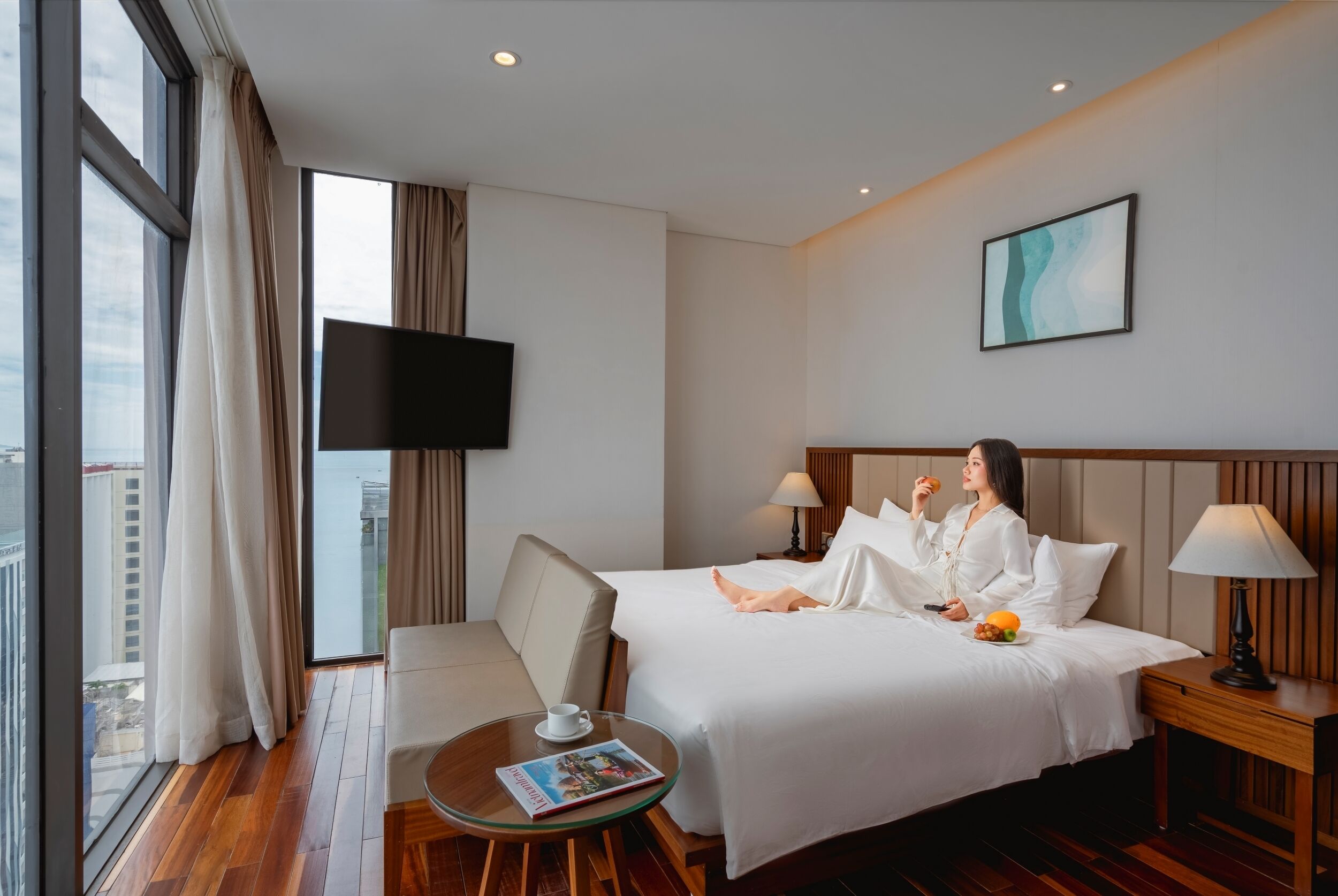 Una habitación de hotel con una cama, una mesita de noche, una silla, una pequeña mesa con una revista y un televisor en la pared.