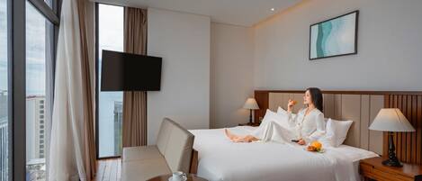 Una habitación de hotel con una cama, una mesita de noche, una silla, una pequeña mesa con una revista y un televisor en la pared.