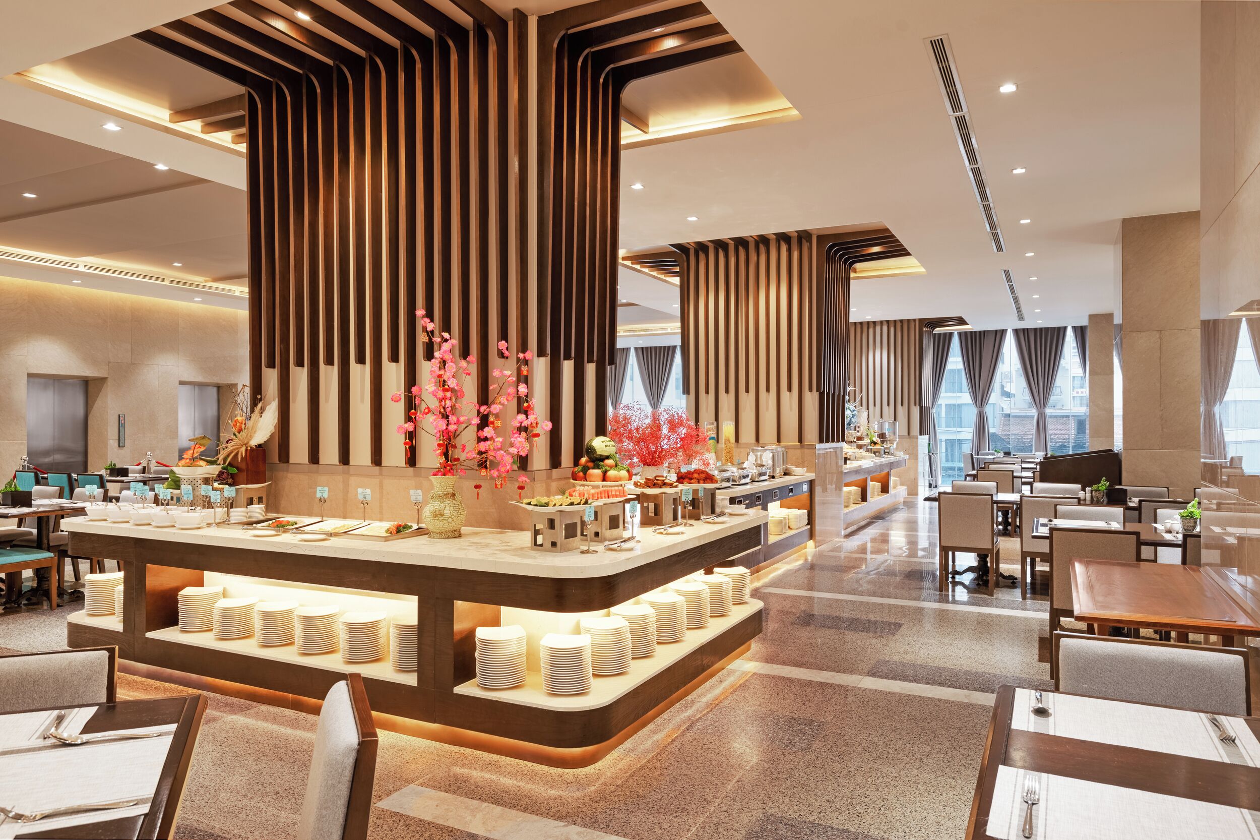 A modern hotel lobby with a central buffet area, seating arrangements, and a large window providing a view of the city.