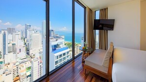 Ein Hotelzimmer mit großem Fenster und Blick auf die Stadt, einem Bett, einem Fernseher und einem kleinen Tisch mit einer Pflanze.