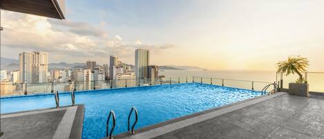 A rooftop pool with a cityscape view, including high-rise buildings and a sunset.