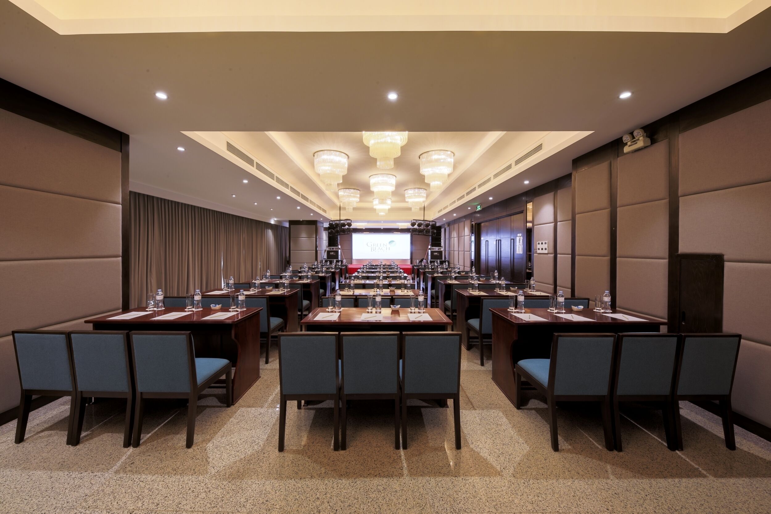 Une salle de conférence dotée de plusieurs tables et chaises, ainsi que de microphones et d’écrans.