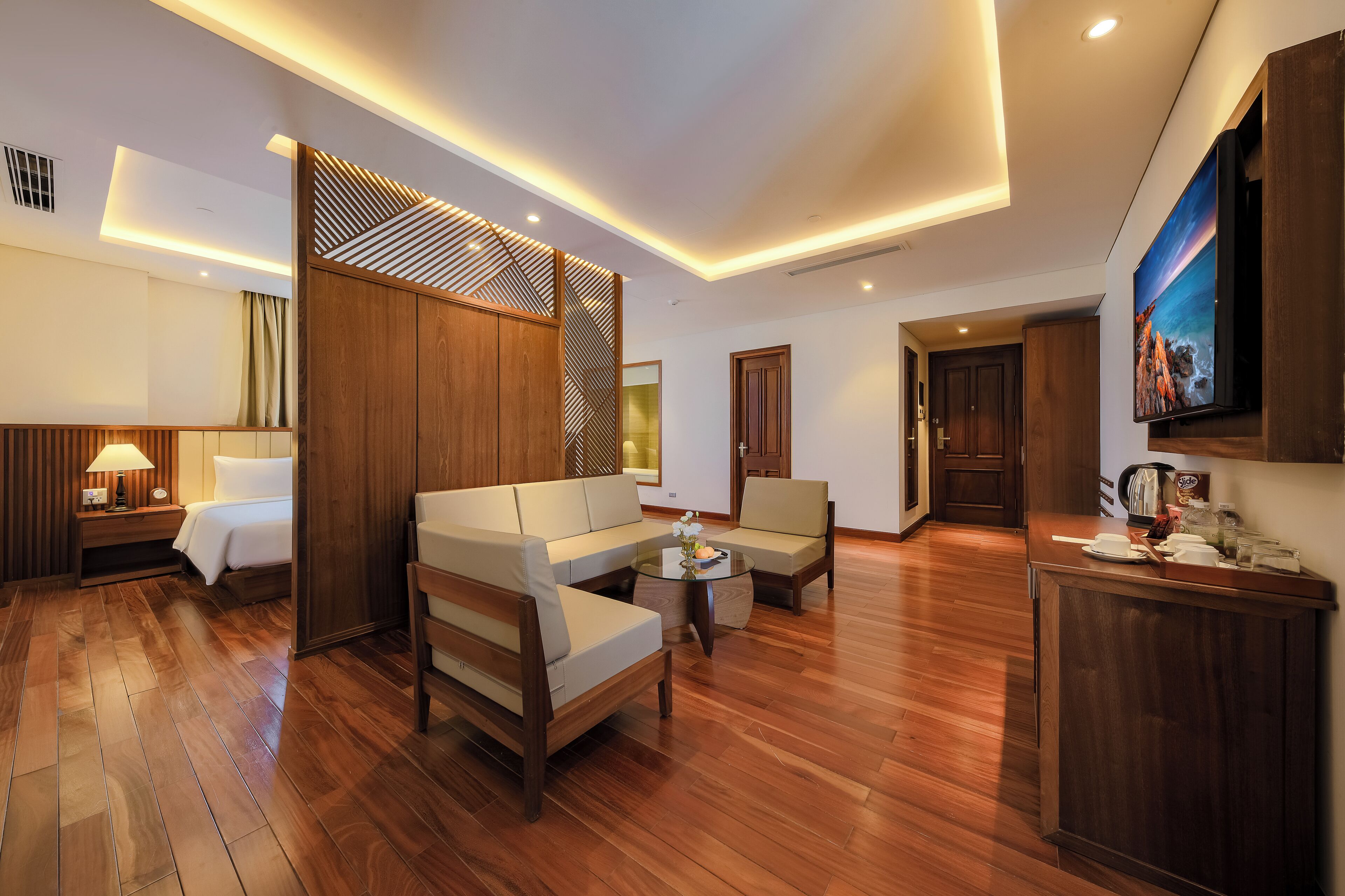 Ein modernes Hotelzimmer mit Holzboden, einer Couch, einem Sessel, einem kleinen Tisch und einem an der Wand befestigten Fernseher.
