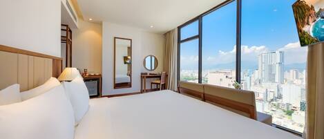 Une chambre d’hôtel avec un grand lit, un bureau, une chaise, un miroir rond et un téléviseur.