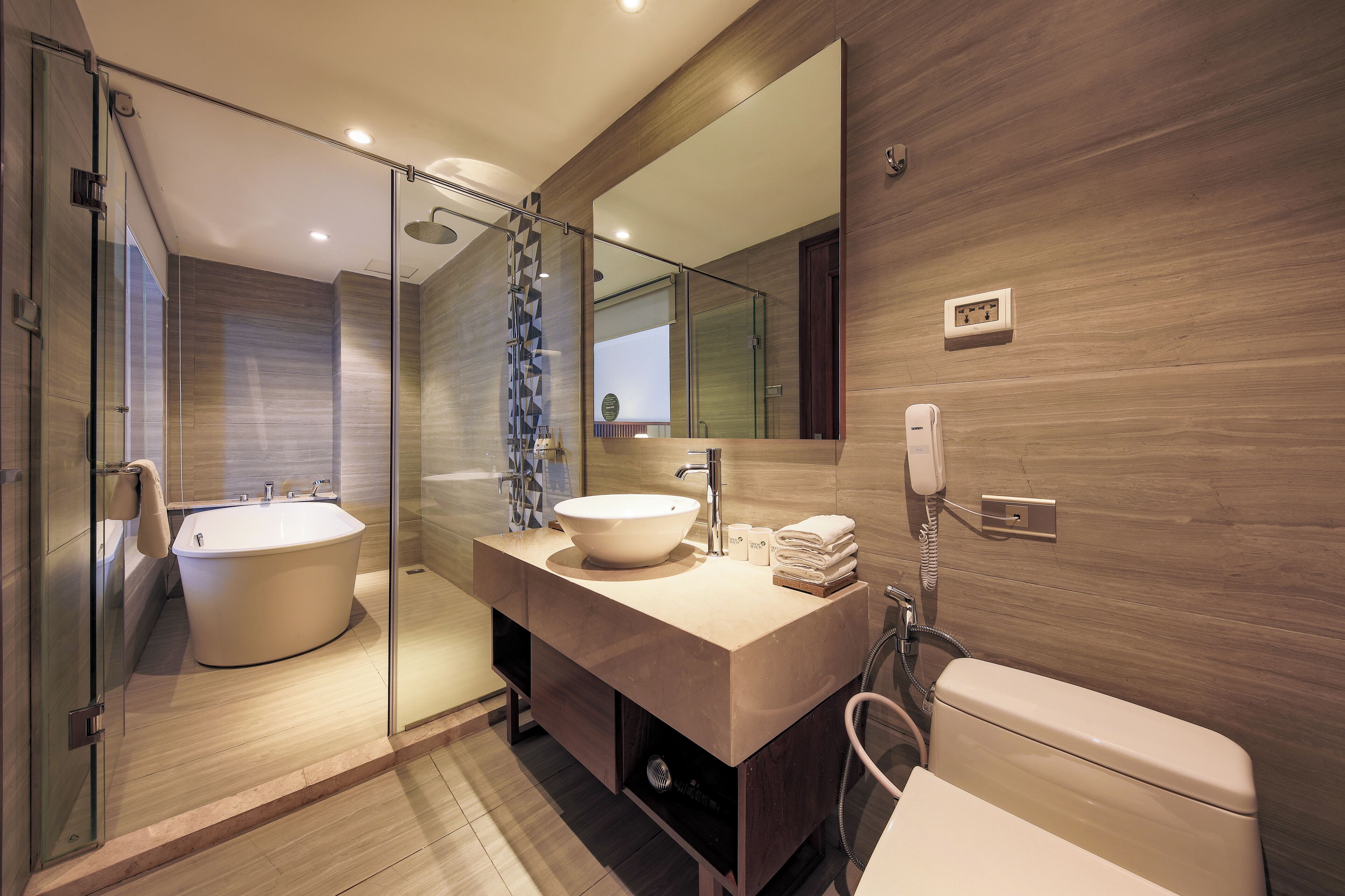 A modern bathroom with a glass-enclosed shower, a freestanding bathtub, a vanity with a large sink, and a toilet.
