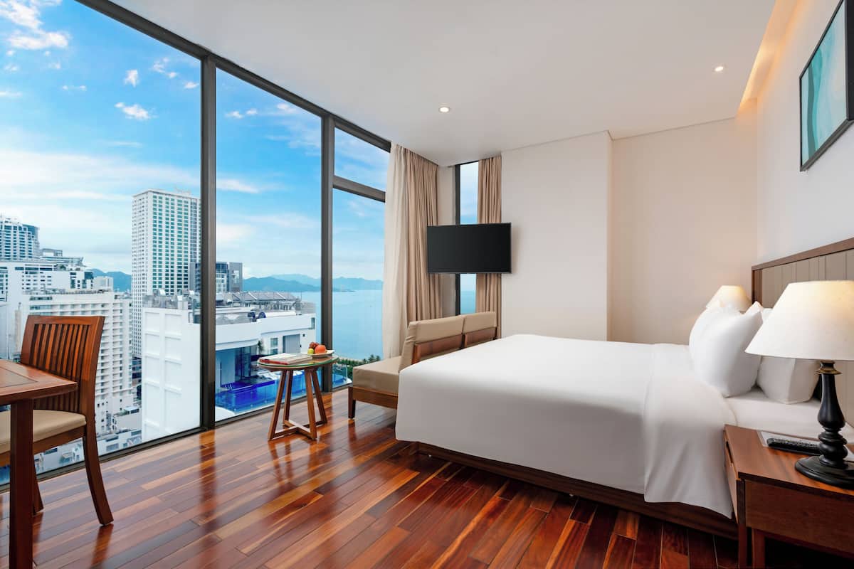 A hotel room with a large window, a bed, a desk, and a chair.