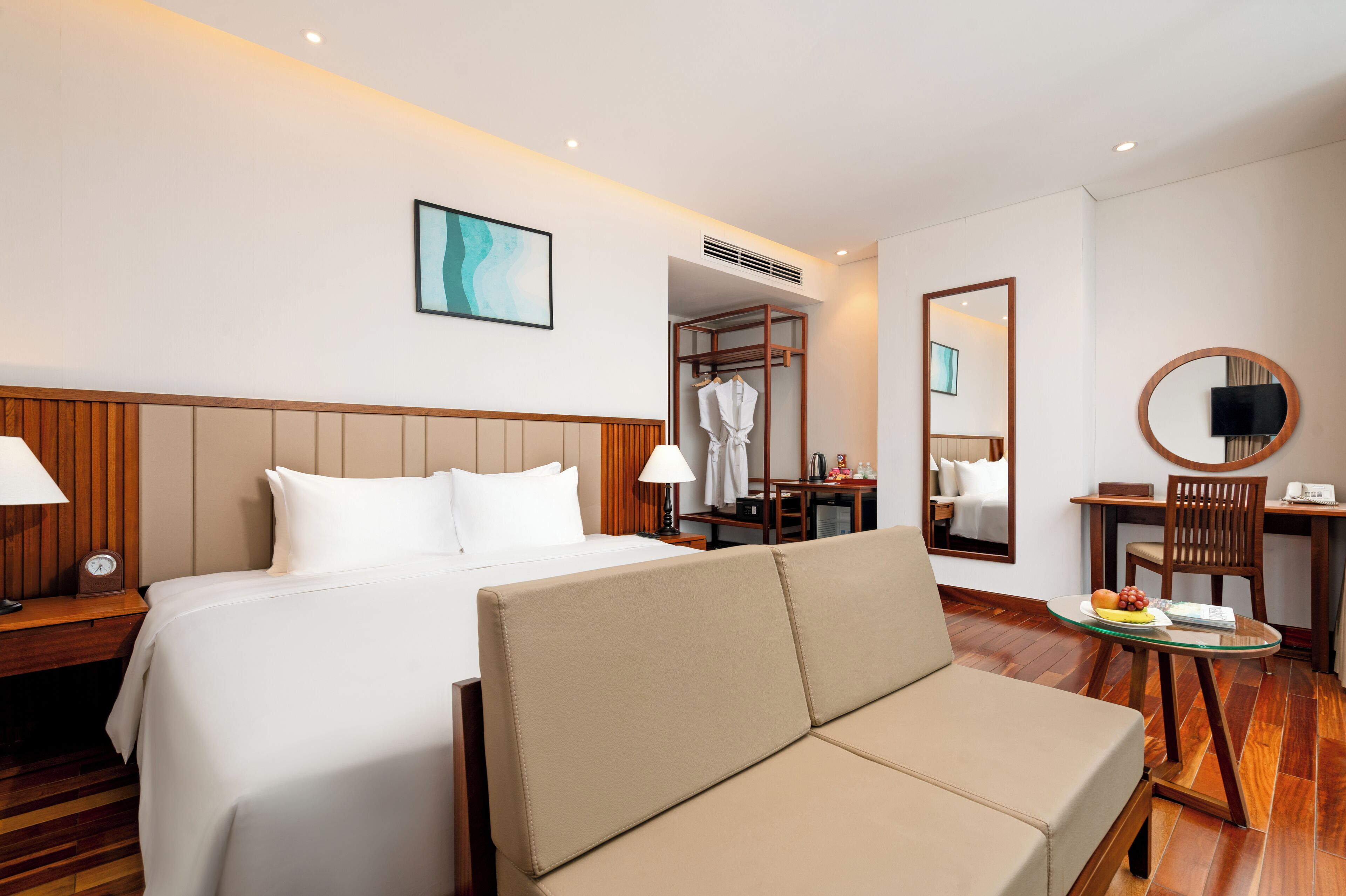 Een hotelkamer met een bed, een slaapbank, een bureau met stoel, een spiegel en een televisie.