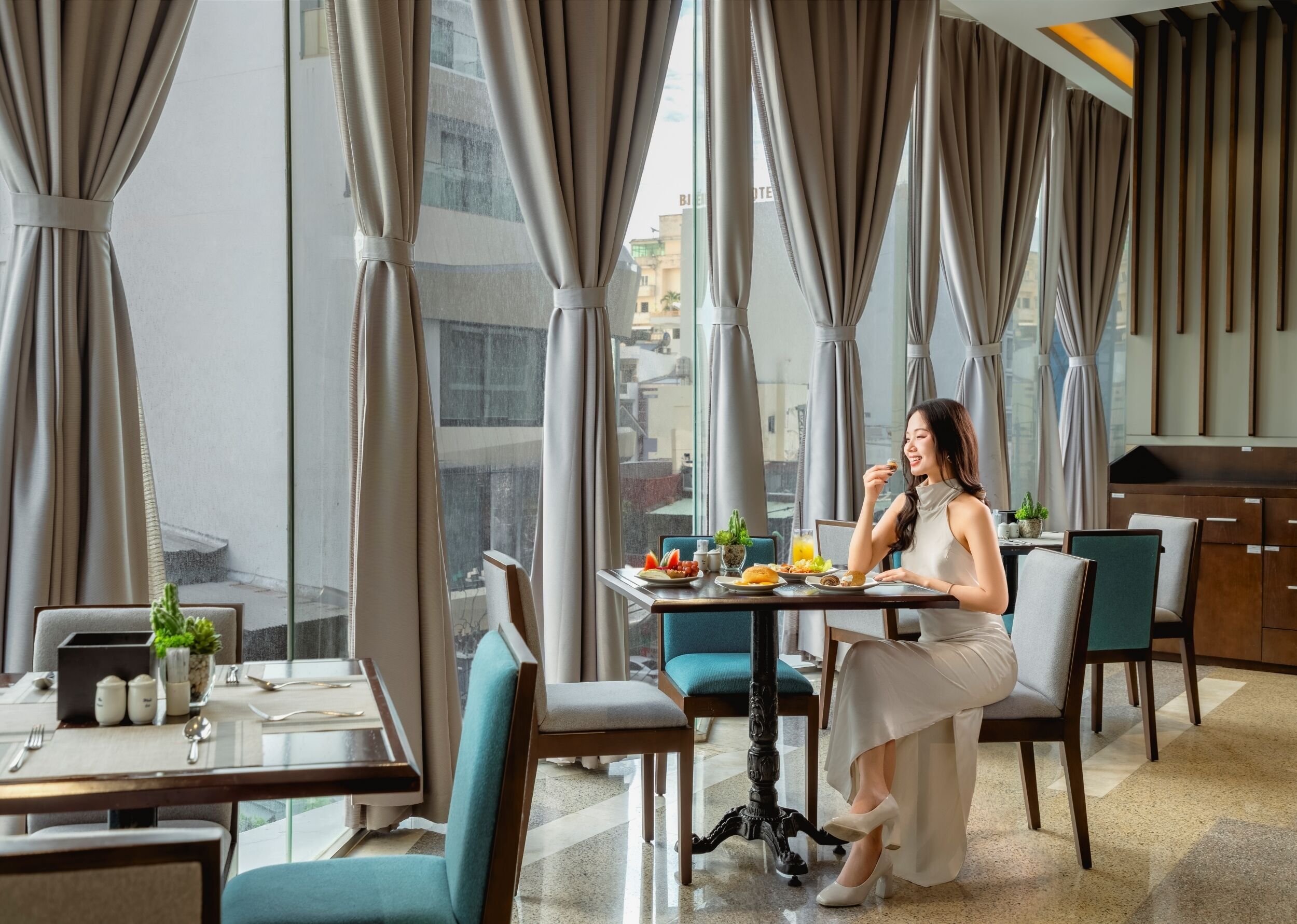 A modern dining area with a large window, a table set with plates, and a person seated.