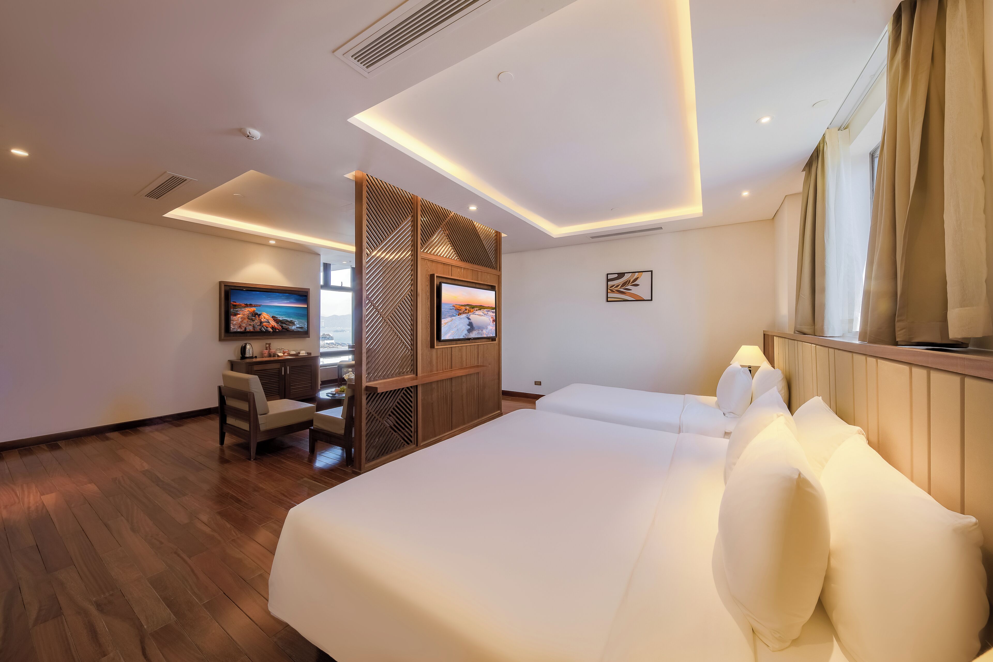 A modern hotel room with a large bed, a desk with a TV, and a wooden partition.