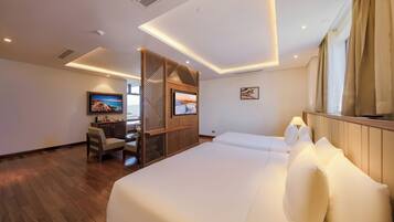 A modern hotel room with a large bed, a desk with a TV, and a wooden partition.