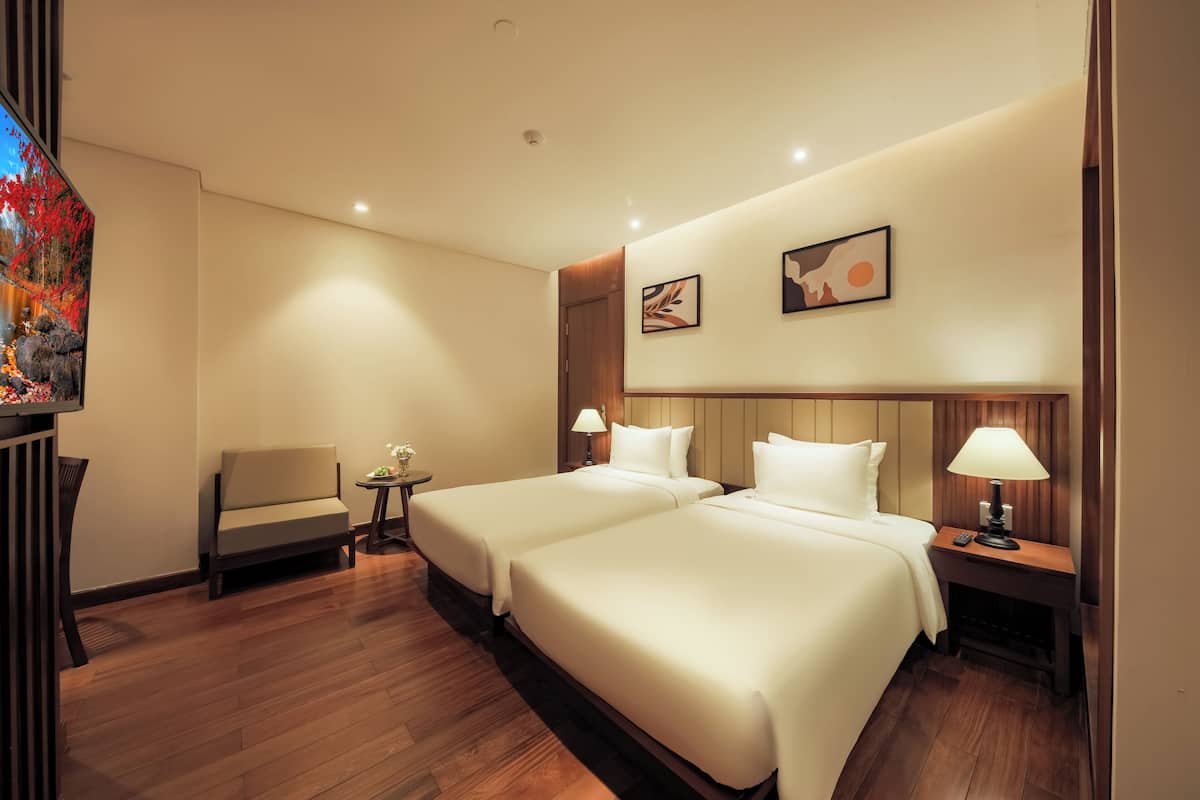 A hotel room with two beds, a sofa, a small table, and a nightstand with a lamp.