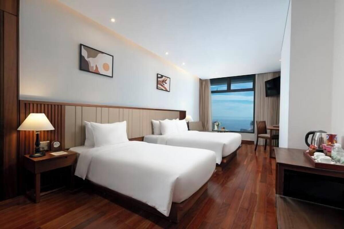 A hotel room with two beds, a desk, a chair, and a large window with a view.