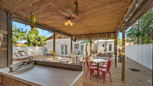 A covered outdoor dining area with a wooden deck, a marble counter, and red chairs.