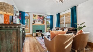 A cozy living room with a fireplace, wooden flooring, and a sofa with cushions.