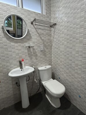 A bathroom with a white tiled wall, a round mirror, a white sink, and a toilet.